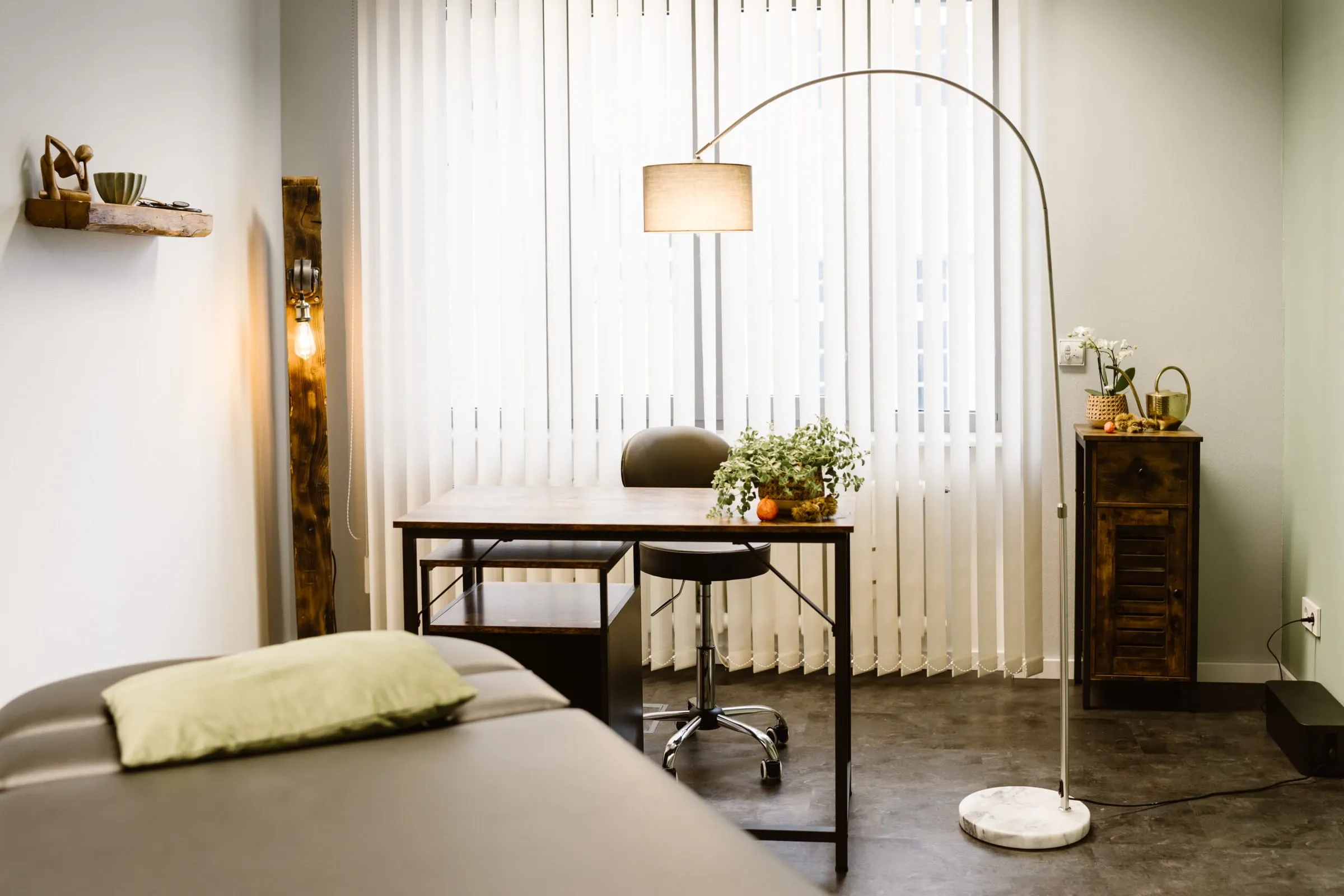 Heller Behandlungsraum mit Liege, Schreibtisch und Pflanzen